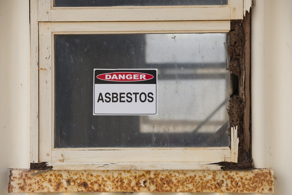 Asbestos danger warning sign on glass window at old rusty toxic contaminated building.